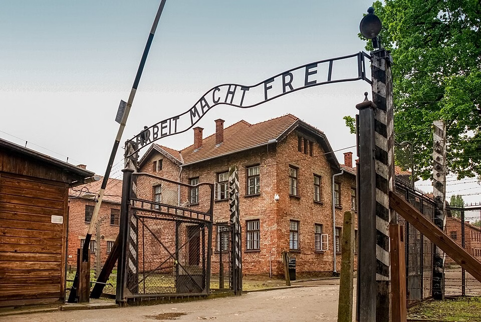 Auschwitz-Birkenau Memorial with historic brick barracks and watchtower under a cloudy sky.