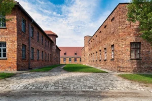 Auschwitz-Birkenau memorial site with barbed-wire fencing, historic barracks, and a quiet overcast landscape.